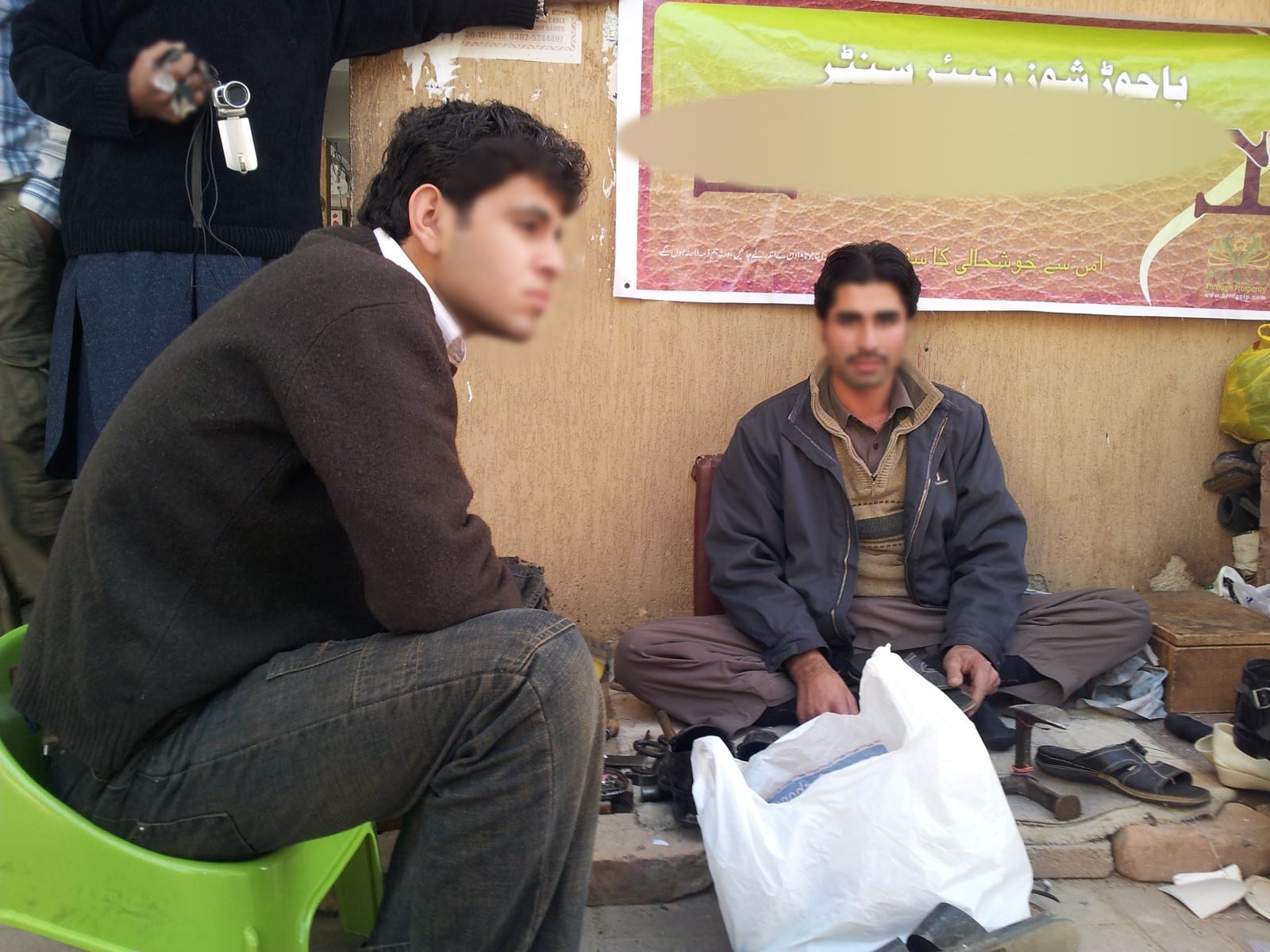 A street cobbler and a Peace Through Prosperity team member beside his stall's new banner, Islamabad, 2013. Faces blurred.