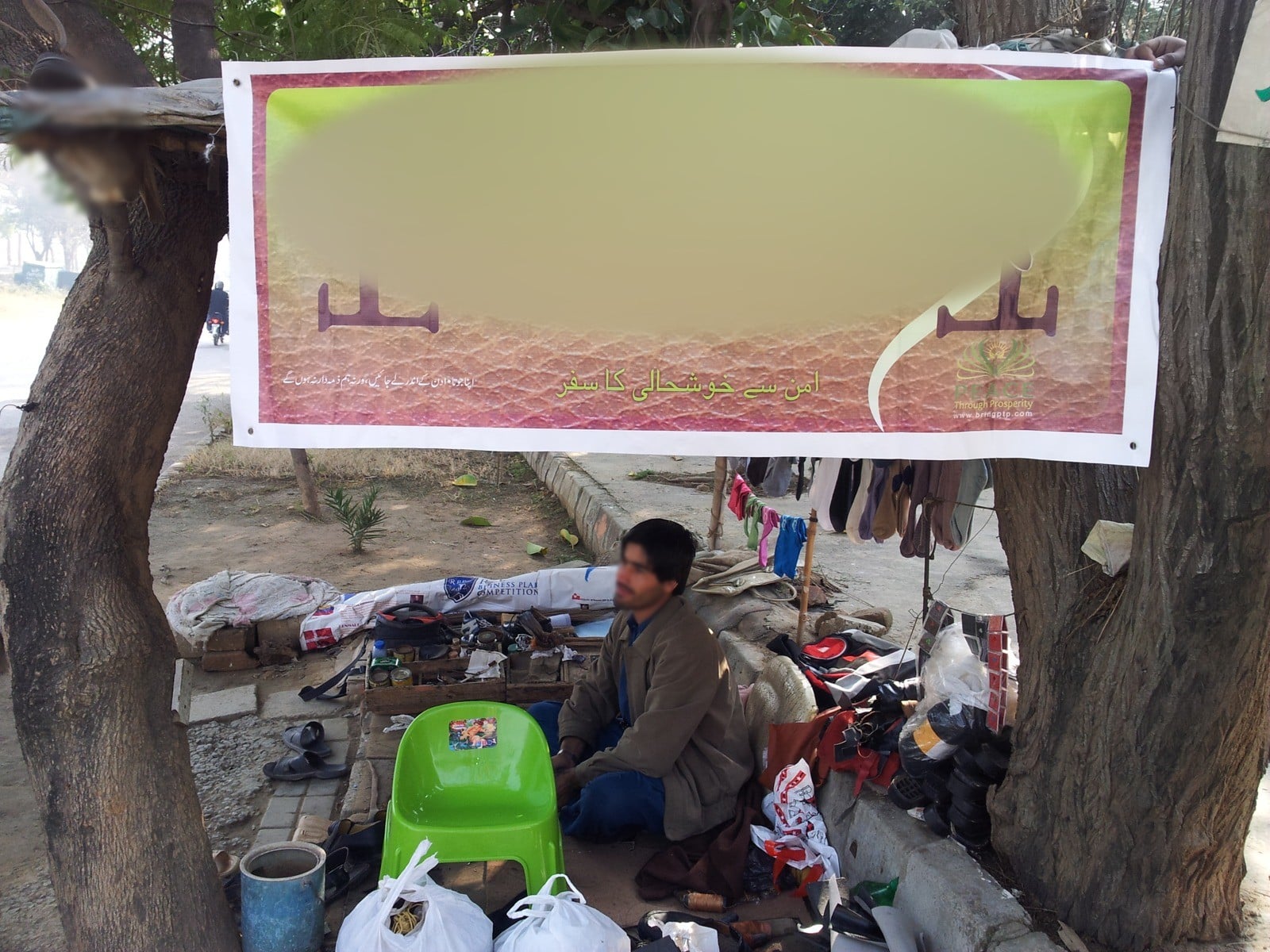 A street cobbler's roadside stall under its new banner, Islamabad, 2013. Face blurred.