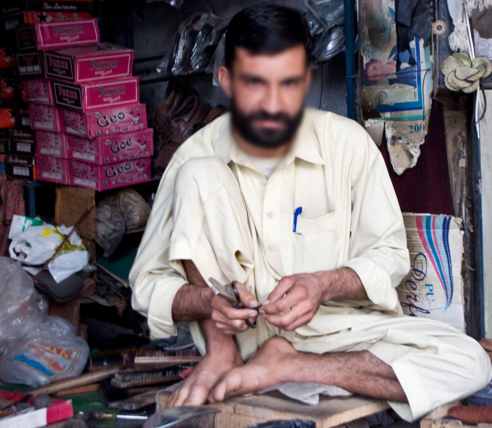 A street cobbler at work in his shop, Pakistan, 2013. Face blurred.