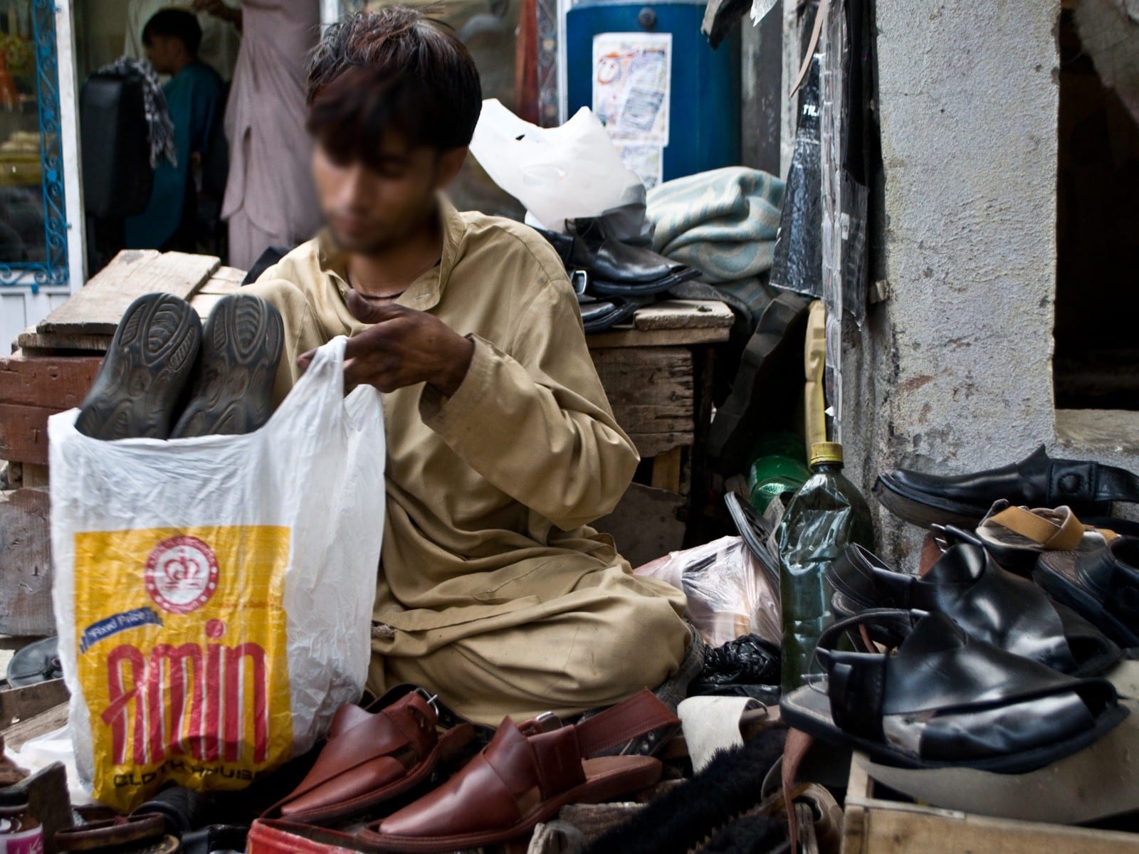 A young street cobbler at work among shoes in Pakistan, 2013. Faces blurred.