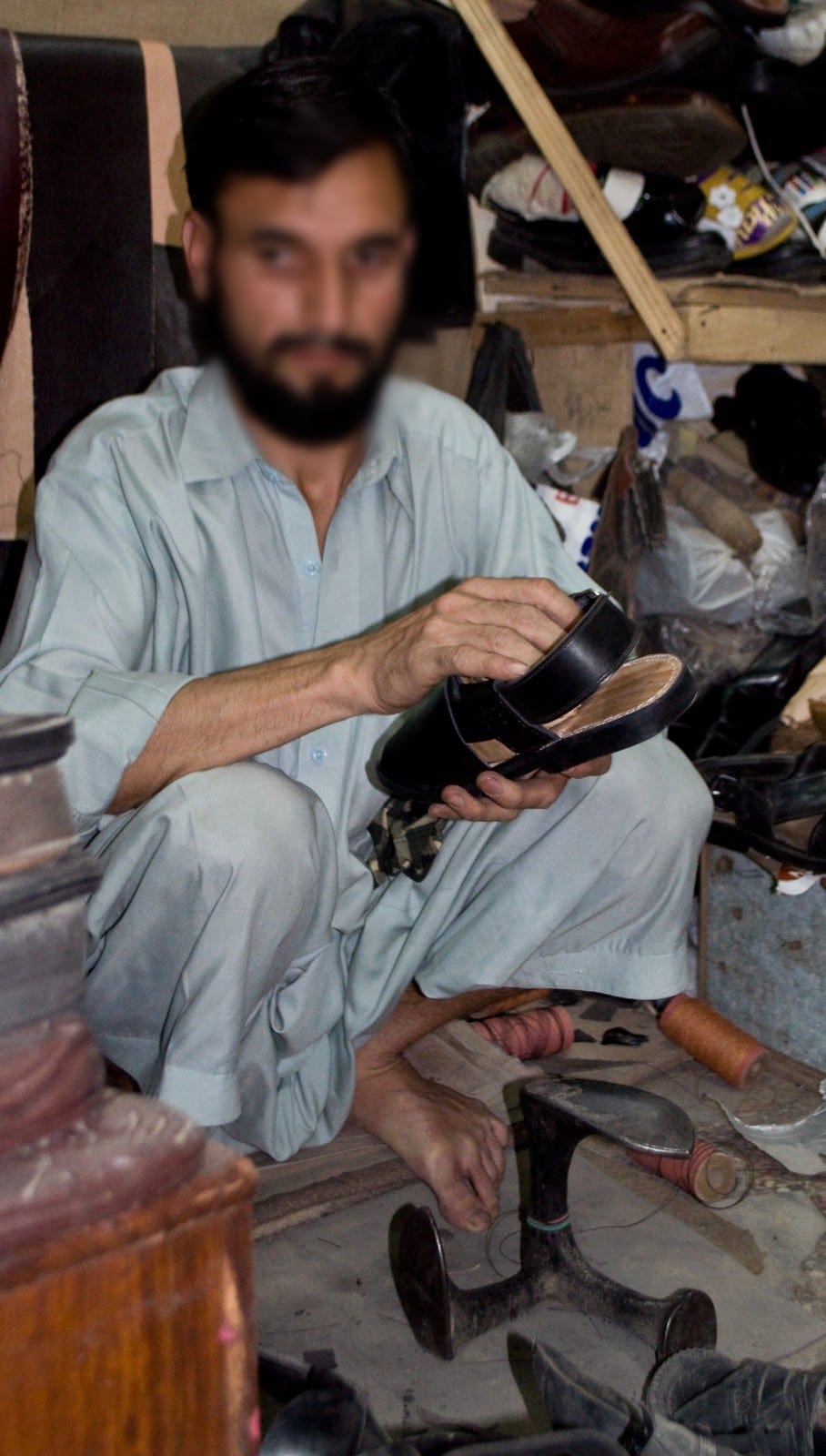 A street cobbler holding a sandal in his stall, Pakistan, 2013. Face blurred.