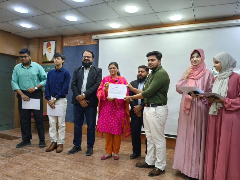 Shahina Noor presenting a Certificate of Completion to a member of Beyond Differences, with the rest of the team and university staff alongside, at Sir Syed University, Karachi
